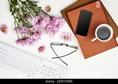 Heller Arbeitsplatz einer Geschäftsfrau. Blumenstrauß mit frischen Frühlingsblumen, Bücher, Smartphone und erfrischender Morgenkaffee auf dem Schreibtisch Stockfoto