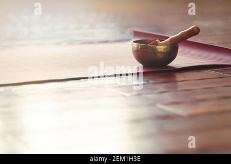 Eine Klangschale steht auf einer Yogamatte auf einem Holzboden mit Kopierfläche. Klangtherapie und Entspannungskonzept. Stockfoto