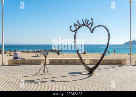 Palmanova, Spanien; februar 20 2021: Seepromenade der mallorquinischen touristischen Ortschaft Palmanova, mit einer eisernen Herzskulptur. Menschen mit einem f Stockfoto