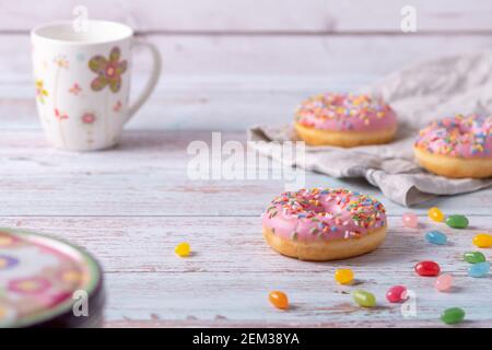 Leckere Donuts mit rosa Glasur, bunten Streuseln und Gelee-Bohnen auf Holzhintergrund. Süßes Gebäck als Snack für Kindergeburtstag. Stockfoto