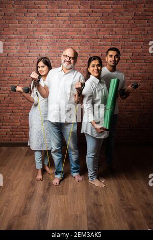 Indische asiatische Familie zu Hause trainieren. Ältere Eltern mit jungen Kindern tun Yoga, Gewichtheben, mit Theraband im Wohnzimmer Innenraum. Indoor-Wor Stockfoto