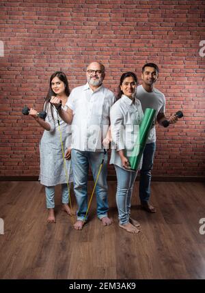 Indische asiatische Familie zu Hause trainieren. Ältere Eltern mit jungen Kindern tun Yoga, Gewichtheben, mit Theraband im Wohnzimmer Innenraum. Indoor-Wor Stockfoto