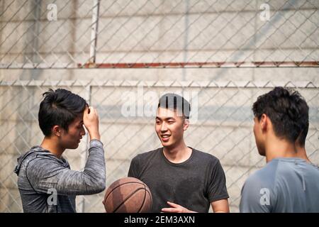 Junge asiatische Basketballspieler unterhalten sich entspannt auf dem Platz im Freien Stockfoto