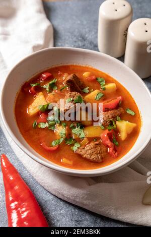 Gulasch ist ein traditionelles ungarisches Gericht mit Rindfleisch, Kartoffeln, Tomaten und Paprika. Gulasch in weißen Tellern mit Gemüse zum Kochen. Stockfoto