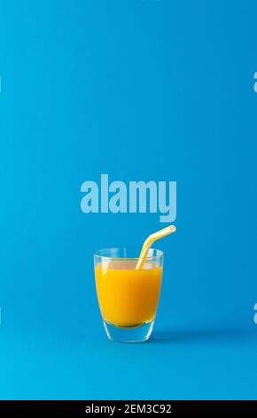 Köstlicher süßer Orangen- oder Mangosaft im Glas mit einem Stroh isoliert auf blauem Hintergrund Stockfoto