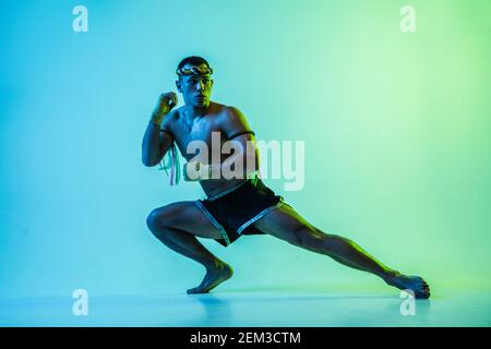 Ein Mann trainiert thai Boxtraining auf blauem Hintergrund in Neonlicht. Stockfoto