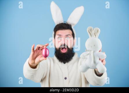 Lustige Hase mit Bart und Schnurrbart halten rosa Ei. Ostersymbol-Konzept. Bärtiger Mann trägt Hasenohren. Eiersuche. Schau, was ich gefunden habe. Hipster niedlichen Hase blauen Hintergrund. Osterhase. Mein Schatz. Stockfoto