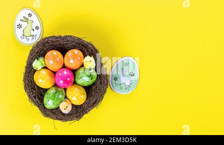 Ostereier im Nest und Holzhäschen auf gelbem Hintergrund. Stockfoto