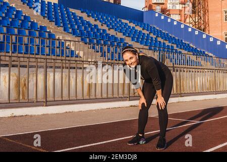 Frau, die sich ausruhte, nachdem sie im Stadion gelaufen war. Fitness lächelnd Frau Portrait Lifestyle in schwarz Trainingsanzug im Freien. Stockfoto