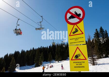 Skipiste, Sessellift, Skifahrer und gelbe Warnschilder am sonnigen Wintertag mit blauem Himmel in Vitosha Berg bei Sofia, Bulgarien, Osteuropa, EU Stockfoto