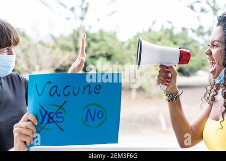 Protesterin Frau demonstriert in Schutzmaske und Banner Meinung für den Impfstoff. Jüngere Mädchen schreien für unterschiedliche Meinung. Stockfoto