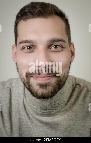 Porträt eines lächelnden jungen braunhaarigen Mannes mit einem kurzen Bart und ein grauer Rollkragenpullover Stockfoto