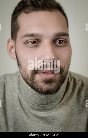 Porträt eines jungen braunhaarigen Mannes mit kurzem Bart Und einen grauen Rollkragenpullover Stockfoto