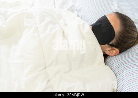 Junge Frau mit Schlafmaske mit weißer Decke bedeckt, liegend im Bett.Insomnia und Schlaf-Konzept Lifestyle mit Kopie Raum für Text. Stockfoto