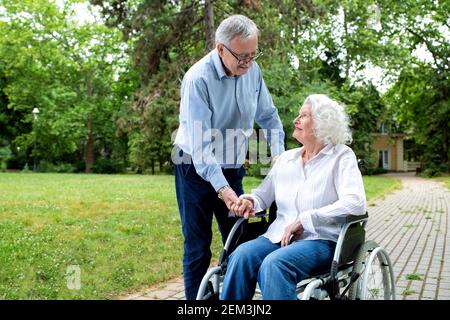 Ältere Frau im Rollstuhl begleitet mit ihrem Mann in der parken Stockfoto