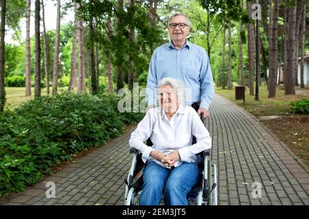 Senior Mann schieben ältere Frau in den Rollstuhl als Sie schreiten durch den Park Stockfoto