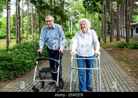 Seniorenpaar, das mit Hilfe von in den Park läuft Gehhilfen Stockfoto