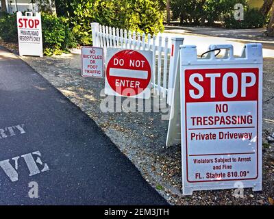 Unfreundliche Straßenschilder warnen davor, eine private Straße zu betreten, die zu teuren Häusern auf Casey Key führt, einer Sperrinsel im Golf von Mexiko im Sarasota County entlang der Westküste Floridas, USA. Die rot-weißen Schilder im Freien versuchen, Fahrzeuge, Radfahrer und Fußgänger daran zu hindern, auf der engen Straße, die gepflegt wird und für die ausschließliche Nutzung der Bewohner entlang ihrer Sackgasse Einfahrt beansprucht wird, einzudringen. Die ultimative Bedrohung für Verletzer ist ein Zeichen, das ein Gesetz zitiert, das Straftäter der Verhaftung und einer Geldstrafe unterstellt. Stockfoto