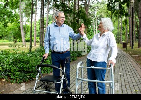 Seniorenpaar im High-Five-Modus bei einem Spaziergang mit Helfern, eine Pause Stockfoto