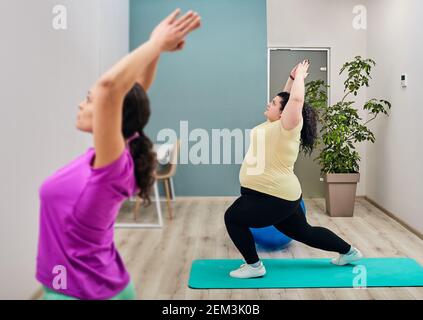 Eine Trainerin führt Training und Stretching für eine übergroße Frau im Fitnessstudio durch. Sportliches Workout zur Gewichtsreduktion Stockfoto