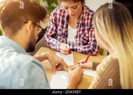 Nahaufnahme von drei fokussierten attraktiven fleißischen High School Schüler sitzen auf den Stühlen in der Bibliothek oder im Klassenzimmer An einem Schreibtisch und Schreiben o Stockfoto