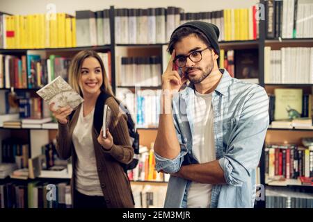 Nahaufnahme von entzückenden niedlichen stilvollen High School Student Mädchen Die Auswahl von Büchern aus einem Bücherregal für einen Freund, während er Stehen verrückt und gelangweilt in der libr Stockfoto