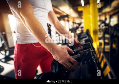 Nahaufnahme Fokus Ansicht der Hände während starke junge muskulöse Bodybuilder Mann ergreifen Hanteln aus der Reihe in der modernen sonnigen Fitnessstudio. Stockfoto