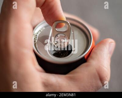 Ziehen der Lasche einer Aluminium-Getränkedose eines Energy Drink mit männlichen Händen auf neutralem Hintergrund Stockfoto