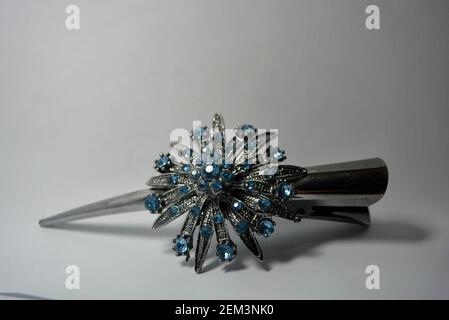 Metall-Haarclip für Frauen mit einer großen metallischen Blume und mit kleinen blauen Steinen verziert und auf einem weißen Hintergrund. Stockfoto