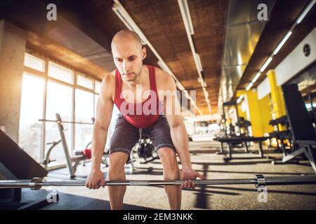 Junge fokussierte fleißige sportliche Fitness-Mann hocken mit Langhantel ohne Gewichte und tun deadlifts in der Turnhalle. Stockfoto