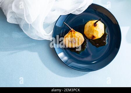 Birnen in Karamellsirup auf einem blauen Teller gebacken, modernes Stillleben. Sommer minimale Komposition mit Birnen auf hellblauem Hintergrund Stockfoto