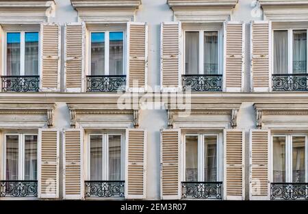 Nahaufnahme der traditionellen französischen Fenster mit offenen Holzfenstern und eleganten schmiedeeisernen Geländern an der Fassade eines Mehrfamilienhauses in Paris. Stockfoto