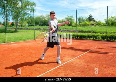 Junger Mann, der auf dem Sandplatz trainiert und Tennis spielt Stockfoto