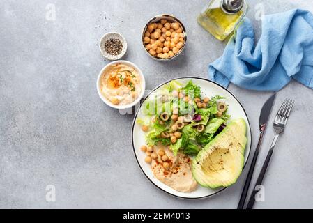 Salat buddha Schüssel mit Kichererbsen, Hummus, Avocado und Grünpflanzen auf grauem Betontisch. Draufsicht, Kopierbereich. Diät, Gewichtsverlust Mahlzeit Konzept Stockfoto