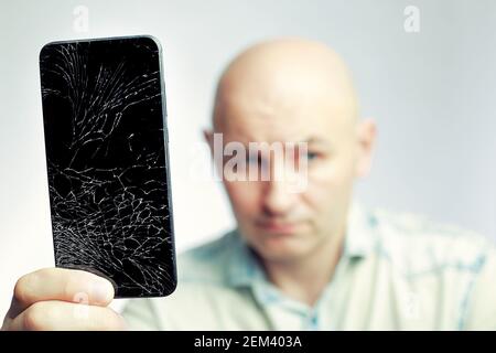 Telefon mit EINEM defekten Bildschirm Nahaufnahme. Ein weißer Mann hält ein schwarzes Smartphone mit einem geknackten Display. Stockfoto