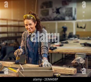 Portrait Ansicht von glücklich attraktiv fleißigen mittleren Alters professionelle Arbeiterin Malerei Holz mit schwarzer Farbe in der sonnigen Werkstatt oder Garage. Stockfoto