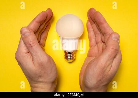 Ein Konzeptbild einer neuen Idee, einer neuen Geburt. Hände Abdeckung LED-Glühbirne. Stockfoto