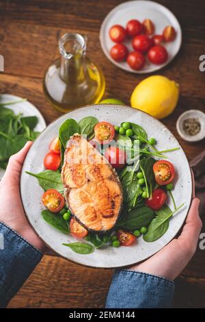 Gegrillter Lachs mit frischem Salat, gesundes Abendessen auf dem Teller in männlichen Händen Stockfoto