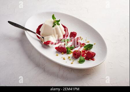 Löffel mit einem Stück Panna Cotta mit Sirup, Himbeeren und Minze in ovaler Platte, Food Stylind, High-Key, close up Stockfoto