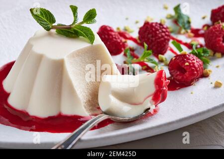 Löffel mit einem Stück Panna Cotta mit Sirup, Himbeeren und Minze in ovaler Platte, Lebensmittel-Stylind, High-Key, close up, Makro, Selektiver Fokus Stockfoto