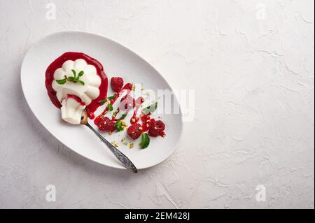 Löffel mit einem Stück Panna Cotta mit Sirup, Himbeeren und Minze in ovaler Platte, Food Stylind, High-Key, Draufsicht Stockfoto