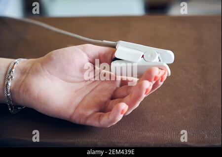 Nahaufnahme der Frau Hand mit Clip-on-Gerät zur Überwachung der Sauerstoffsättigung und Pulsfrequenz. Patientin mit Pulsoximeter am Daumen. Konzept der Medizin, Gesundheitswesen und Pulsoxymetrie. Stockfoto