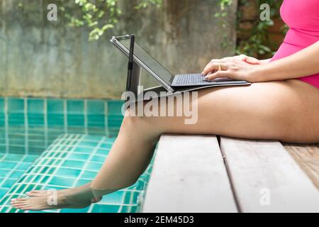 Frau in pinkem Badeanzug, die am Pool am Laptop arbeitet. Stockfoto