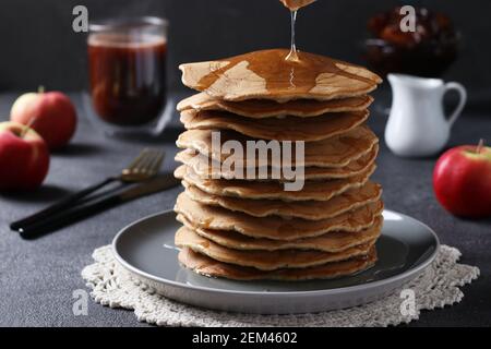 Hausgemachte, üppige Pfannkuchen mit Äpfeln, die mit süßem Sirup übergossen werden Auf einem dunklen Hintergrund Stockfoto