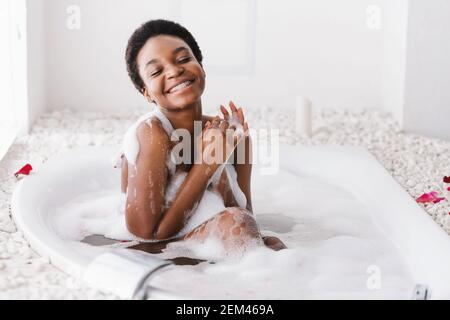 Frau mit geschlossenen Augen des Vergnügens Baden mit Schaum Und Blütenblätter zu Hause Stockfoto