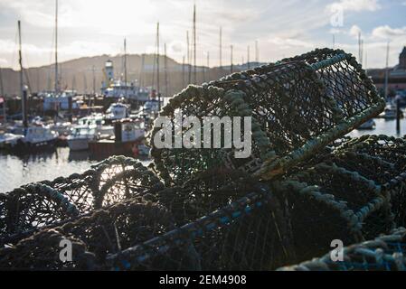 Hummertöpfe stapelten sich in einem Stapel auf einem Hafen Kai des Fischerhafens mit Leuchtturm im Hintergrund Stockfoto