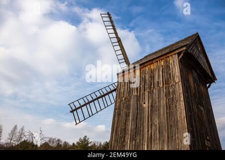 Hölzerne Windmühle in einem ländlichen Freilichtmuseum vor dem Hintergrund des blauen Himmels. Natürliche Lichtverhältnisse. Stockfoto