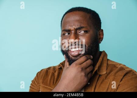 Nachdenklicher junger afrikanischer Mann isoliert auf blauem Hintergrund, Nahaufnahme Stockfoto