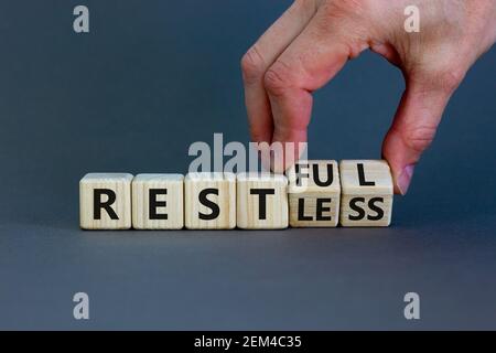 Symbol „Restless“ oder „RESTful“. Geschäftsmann dreht Holzwürfel, ändert das Wort "stlos" in "stful". Schöner grauer Tisch, grauer Hintergrund, Kopierer Stockfoto