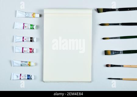 Kunstbedarf. Pinsel und Ölfarben um das leere Notizbuch herum Stockfoto